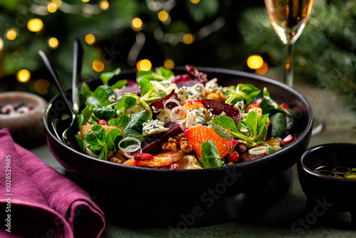 Christmas table with food. Winter salad with beetroot, oranges, walnuts, pomegranate, dried cranberries, lettuce, blue cheese. Pink wine in glass. Honey and olive oil dressing. Christmas tree. photo