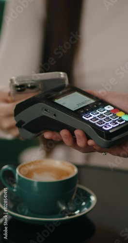Customer paying for order in the cafe with payment terminal using NFC smartphone technology. Close-up girl applying mobile phone on cash machine.