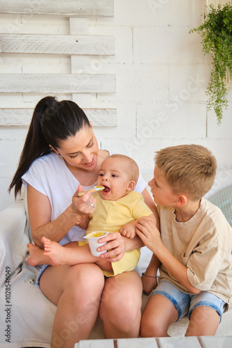 Mother feeding baby while older child watches photo