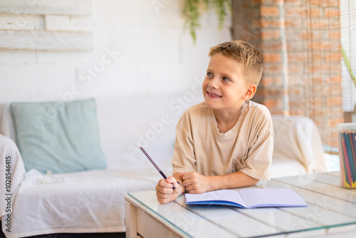 Happy young boy writing in notebook at a bright home setting photo