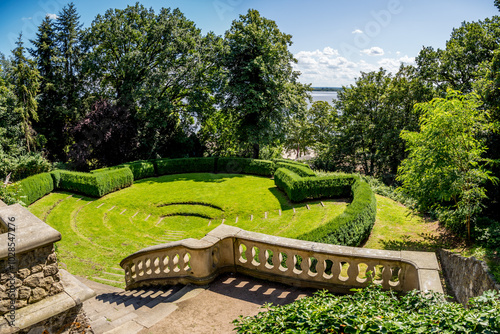 Römischer Garten in Blankenese showcases a stone staircase leading to a grassy area with an inviting open-air stage surrounded by hedges and view of the Elbe River ideal for outdoor events in Hamburg.