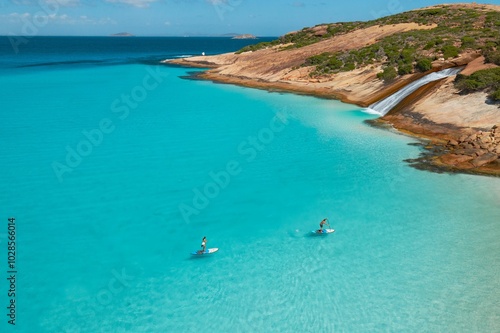 Aerial view of paddleboarding in turquoise waters near rocky coastline.