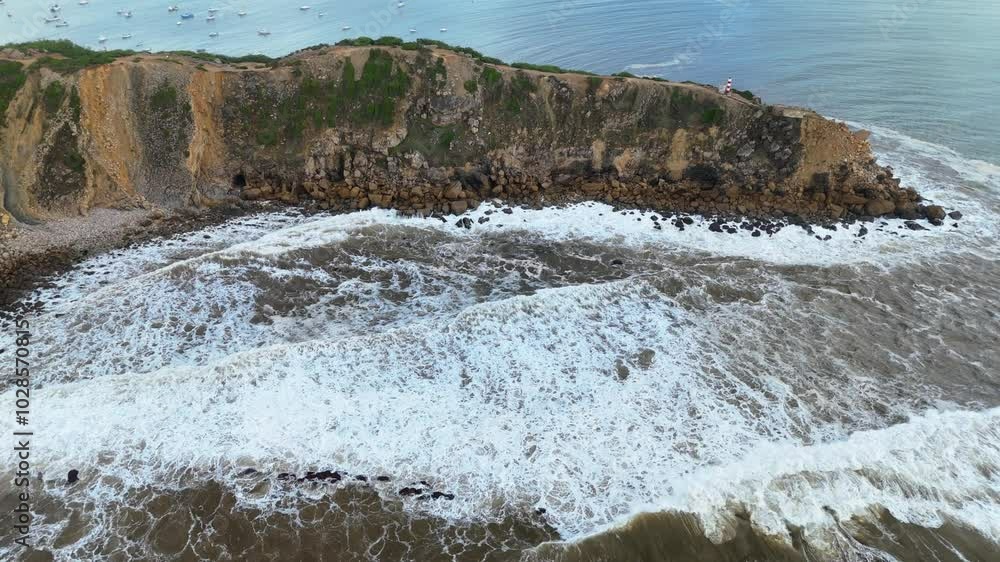 Waves crashing against coastal cliffs near tranquil waters and boats during a sunny day at the beach in Portugal Waves crashing against coastal cliffs near tranquil waters and boats during a sunny day at the beach in Portugal