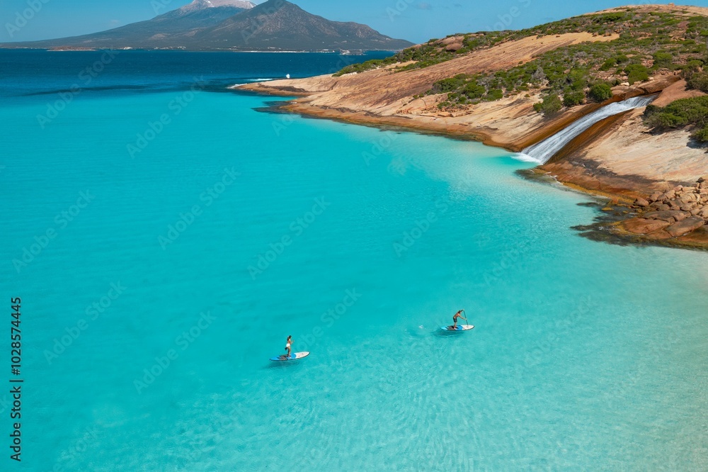Fototapeta premium Paddleboarding in crystal clear turquoise waters near scenic coastal landscape.