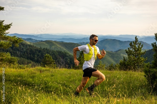 Man jogging on a grassy hill with a scenic view of mountains in the background on a sunny day.