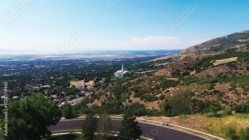 Drone flying above green hills landscape, to reveal bountiful Utah Temple with a nearby road