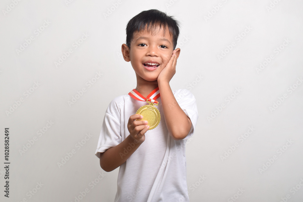 Happy expressive little asian boy with a first place gold medal isolated on a white background. The child celebrating his success Happy expressive little asian boy with a first place gold medal isolated on a white background. The child celebrating his success