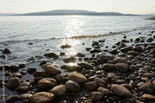 Serene lakeshore with stones and sunlight reflections