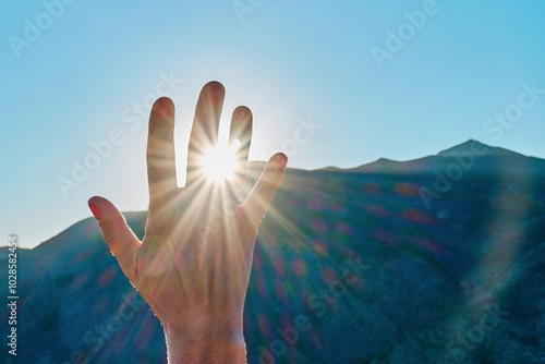 Touching the sun. Anonimus hand covering sunlight, bright sun's rays pass through the fingers over mountain background. photo