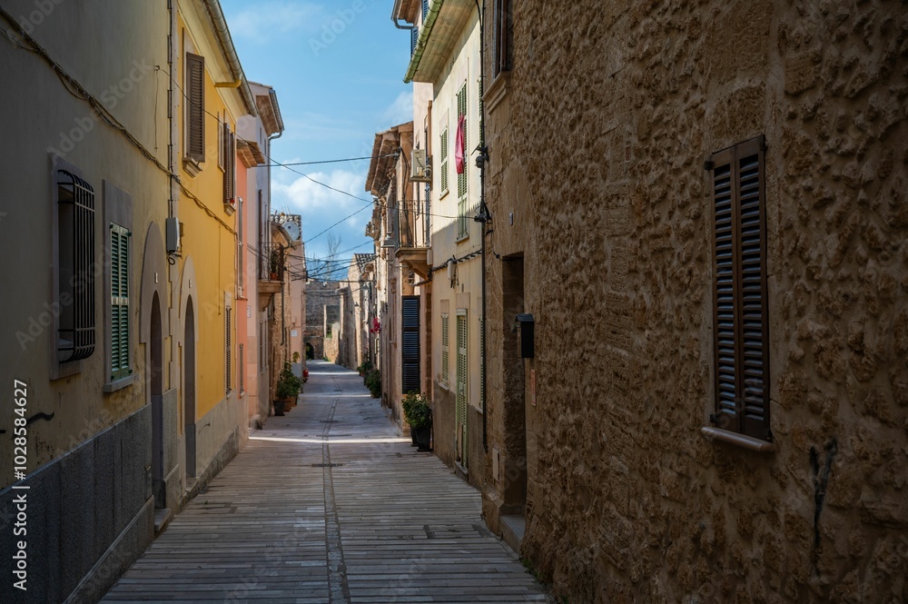 Obraz premium Narrow alleyway in a village with colorful buildings and a clear blue sky in Alcudia, Mallorca