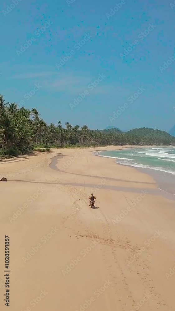 Drone vertical view of a person riding bike on a sandy beach on a sunny bright day with blue sky Drone vertical view of a person riding bike on a sandy beach on a sunny bright day with blue sky