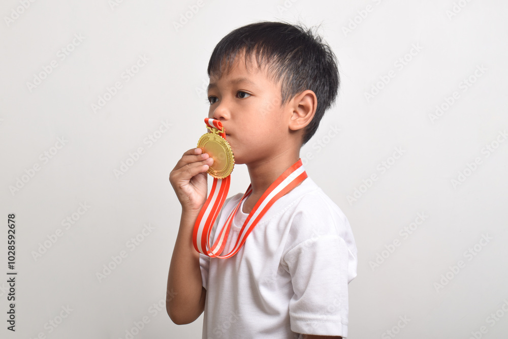 Gold Medal. Asian boy kissing a gold medal isolated on a white background. The boy celebrating his victory. Sports trophy for the first place Gold Medal. Asian boy kissing a gold medal isolated on a white background. The boy celebrating his victory. Sports trophy for the first place