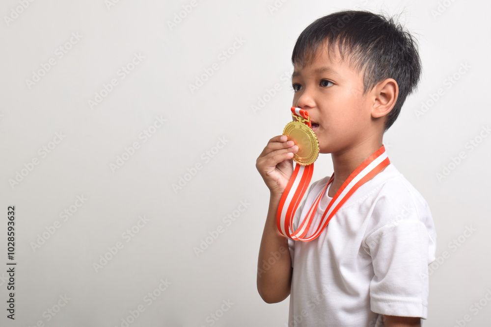 Gold Medal. Asian boy kissing a gold medal isolated on a white background. The boy celebrating his victory. Sports trophy for the first place Gold Medal. Asian boy kissing a gold medal isolated on a white background. The boy celebrating his victory. Sports trophy for the first place