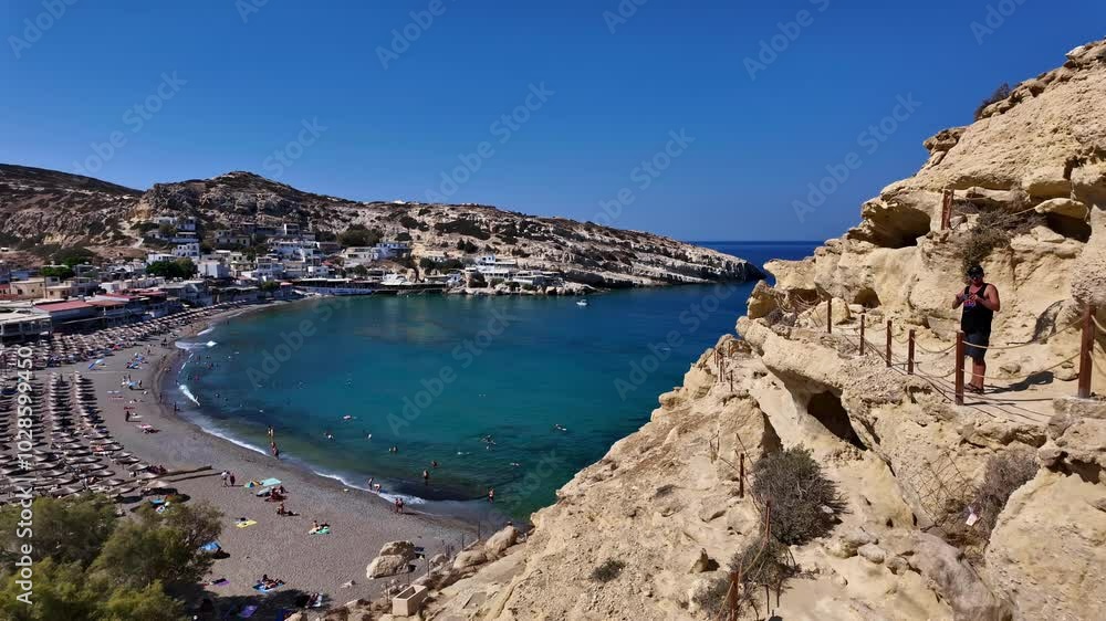 Climber explores ancient Matala Caves overlooking turquoise bay on a sunny day in Greece Climber explores ancient Matala Caves overlooking turquoise bay on a sunny day in Greece