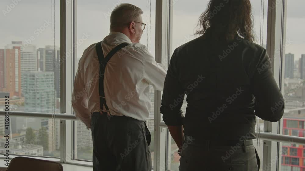 An older CEO harshly explains something to one of his employees in an office overlooking a city skyline An older CEO harshly explains something to one of his employees in an office overlooking a city skyline