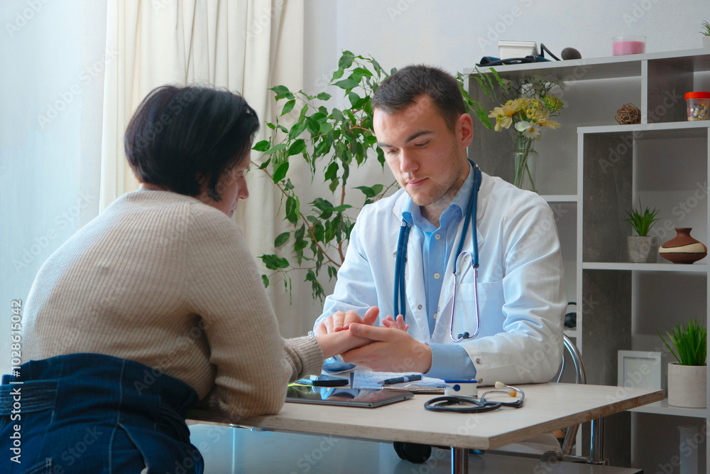 Fototapeta premium An elderly doctor, at his workplace, receives patients. He examines a disabled woman, missing finger phalanges.