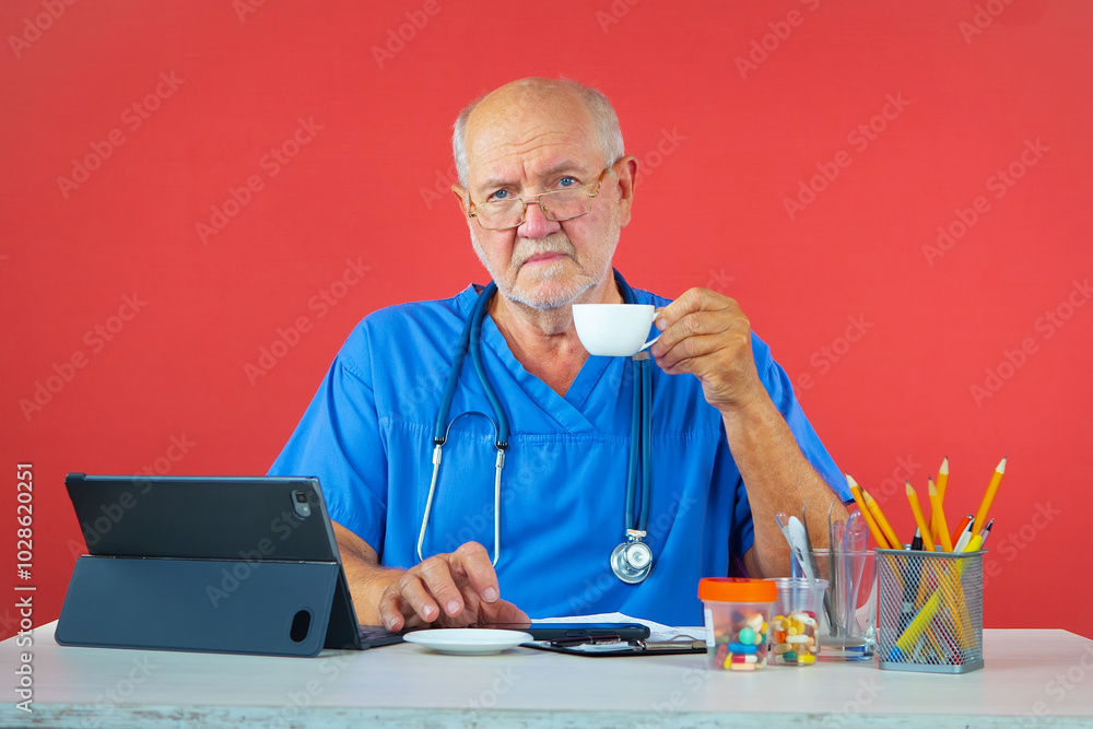 An elderly man, a doctor, in his office, at the table. Blue background. An elderly man, a doctor, in his office, at the table. Blue background.