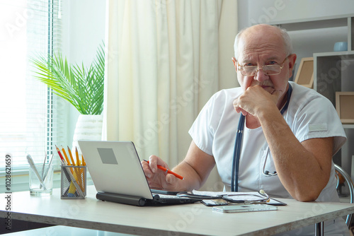 An elderly man, a doctor, in his office, at a table.