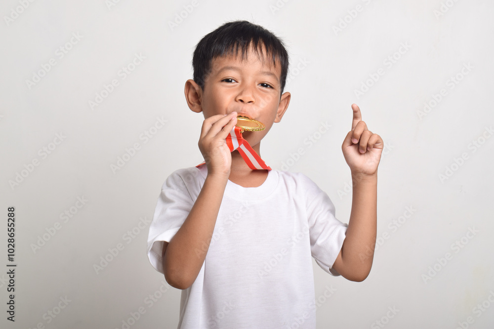 Asian boy biting the gold medal and showing a thumbs up isolated on a white background. First place winner after competition Asian boy biting the gold medal and showing a thumbs up isolated on a white background. First place winner after competition