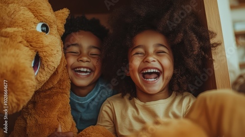 Two joyful children share infectious laughter as they play with a teddy bear, capturing a heartwarming moment of friendship and playful innocence.