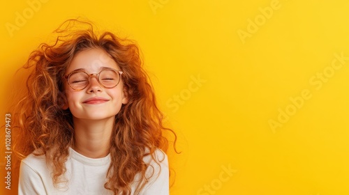 A girl with curly hair and glasses smiles blissfully with closed eyes, set against a bold yellow background, capturing a moment of pure contentment.