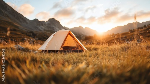 A solitary tent resides quietly amidst an expansive mountainscape as the sun sets, casting golden hues across the open field, creating a tranquil camping setting. photo