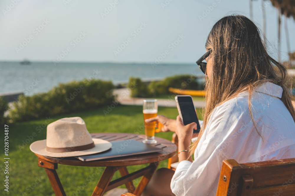 Obraz premium A woman is sitting at a table by the ocean, remote work concept