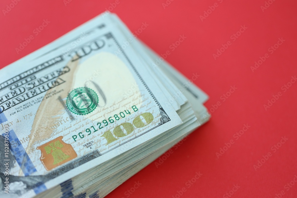Big amount of hundred dollar bills in thick stack lies on bright red color paper background Big amount of hundred dollar bills in thick stack lies on bright red color paper background