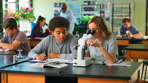Male And Female High School Students Using Microscope In Biology Class