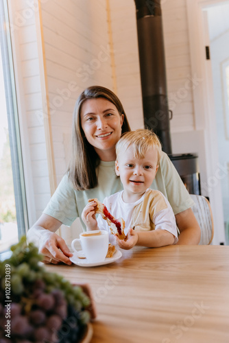 Mother and child enjoying breakfast with coffee and croissants in kitchen, sharing a peaceful moment photo