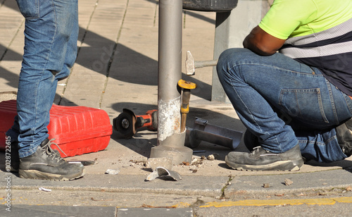 People working on maintenance of exterior properties on public roads, repairing a pole on a sidewalk on a city street