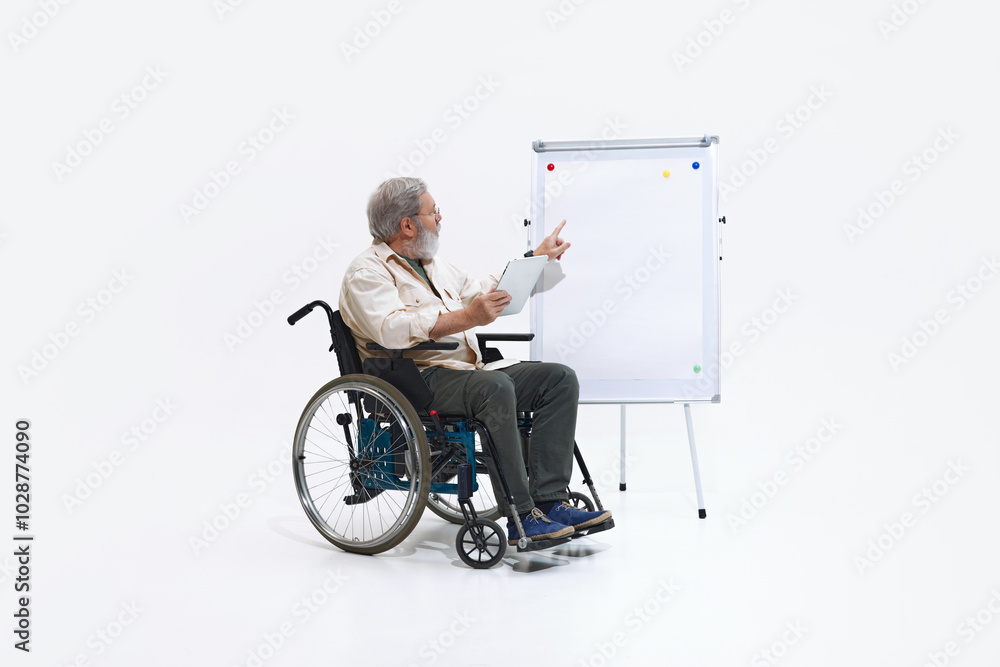 Smart elderly man sitting in wheelchair near flipchart and conducting analysis, working against white studio background. Concept of DEI, business, partnership, work, support and unity. Smart elderly man sitting in wheelchair near flipchart and conducting analysis, working against white studio background. Concept of DEI, business, partnership, work, support and unity.