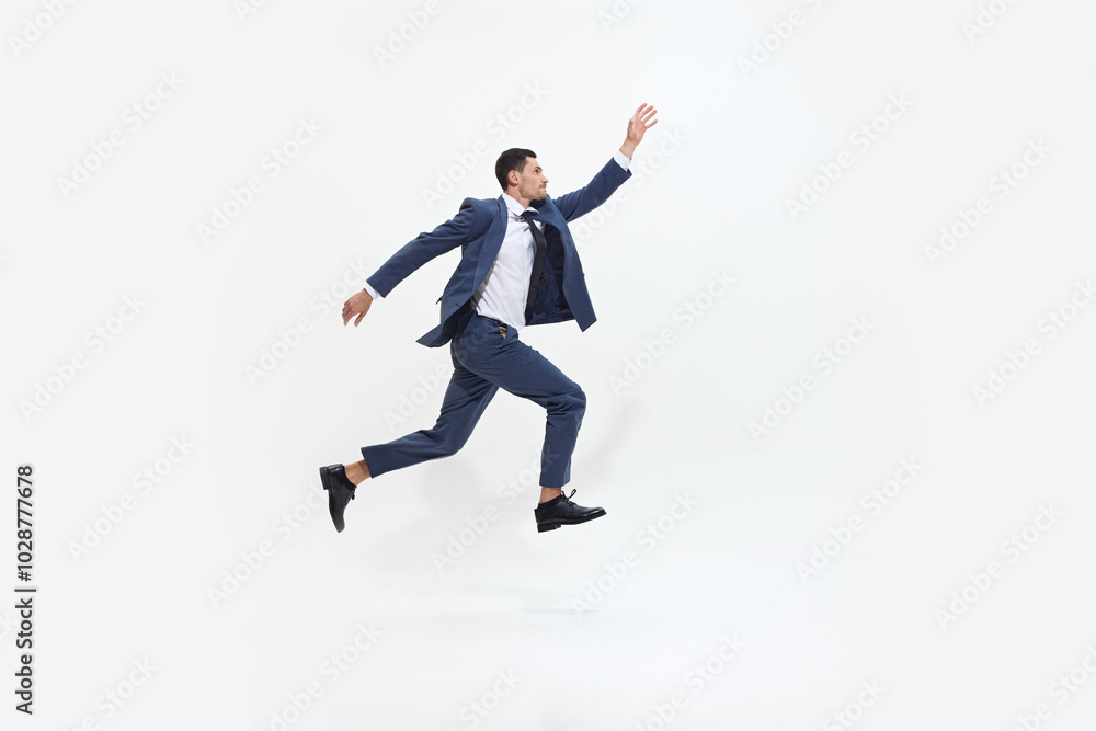 Man in suit runs energetically with determined expression, in mid-air as if striving towards something against white studio background. Concept of DEI, business, partnership, work, support and unity. Man in suit runs energetically with determined expression, in mid-air as if striving towards something against white studio background. Concept of DEI, business, partnership, work, support and unity.