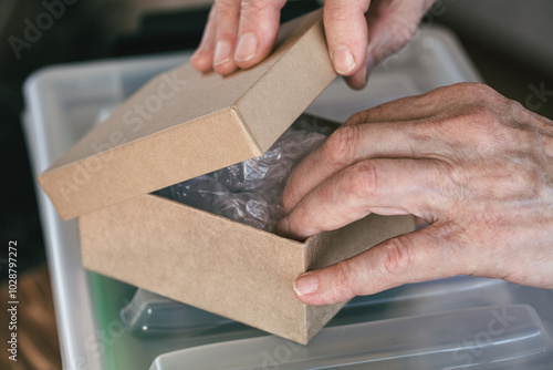 Elderly female hands getting the package out of small cardboard box, close-up, selective focus.