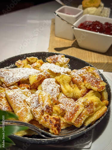 Famous Austrian sweet dish Kaiserschmarrn served in a pan with ice cream, raspberry and stewed plums