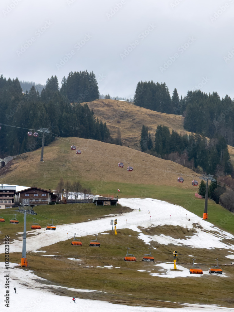 Very bad and poor snow conditions in alpine ski region of Saalbach-Hinterglemm at the end of the season in March 2024 against cloudy sky
