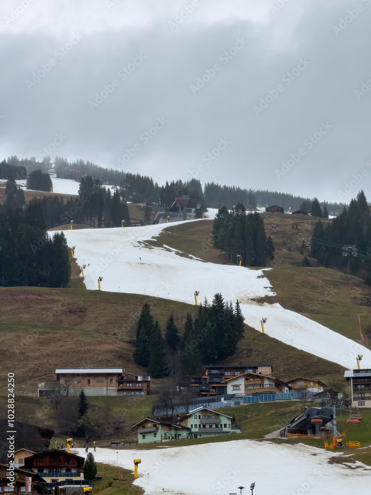 Very bad and poor snow conditions in alpine ski region of Saalbach-Hinterglemm at the end of the season in March 2024 against cloudy sky