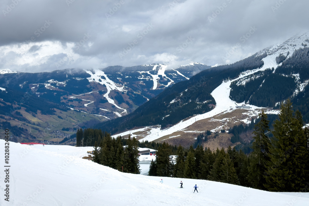 Scenic view of ski region of Saalbach-Hinterglemm and slopes in bad conditions in the Austrian alps against cloudy sky in mid March 2024