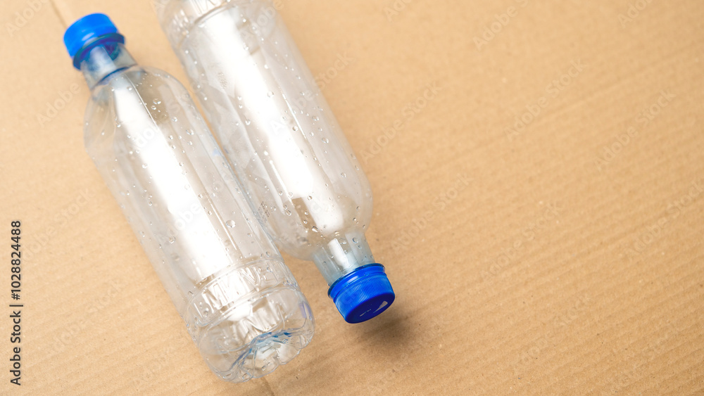 Naklejka premium Two plastic bottles with blue caps on a brown surface. The bottles are empty and appear to be discarded
