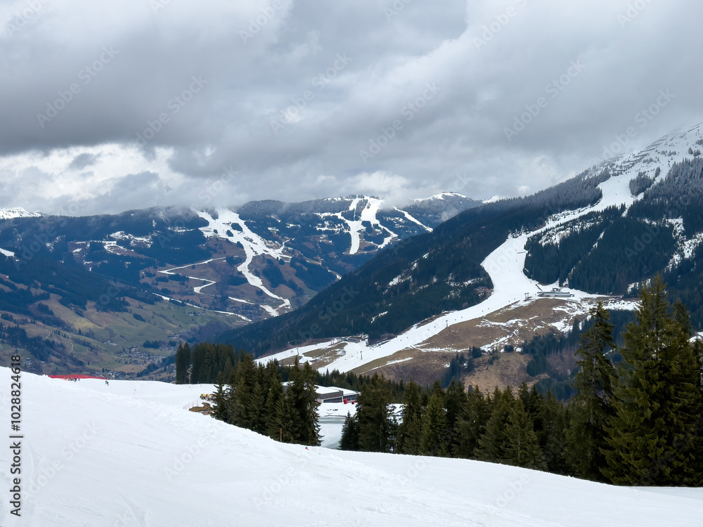 Scenic view of ski region of Saalbach-Hinterglemm and slopes in bad conditions in the Austrian alps against cloudy sky in mid March 2024