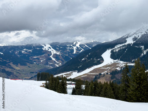 Scenic view of ski region of Saalbach-Hinterglemm and slopes in bad conditions in the Austrian alps against cloudy sky in mid March 2024