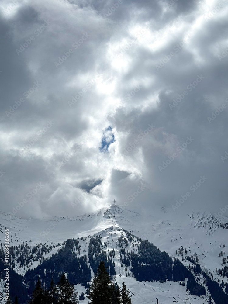 Electric power line runnnig up a snow covered mountain with snow line at the bottom in the ski region of Saalbach-Hinterglemm, Austria against dramatic cloudy sky
