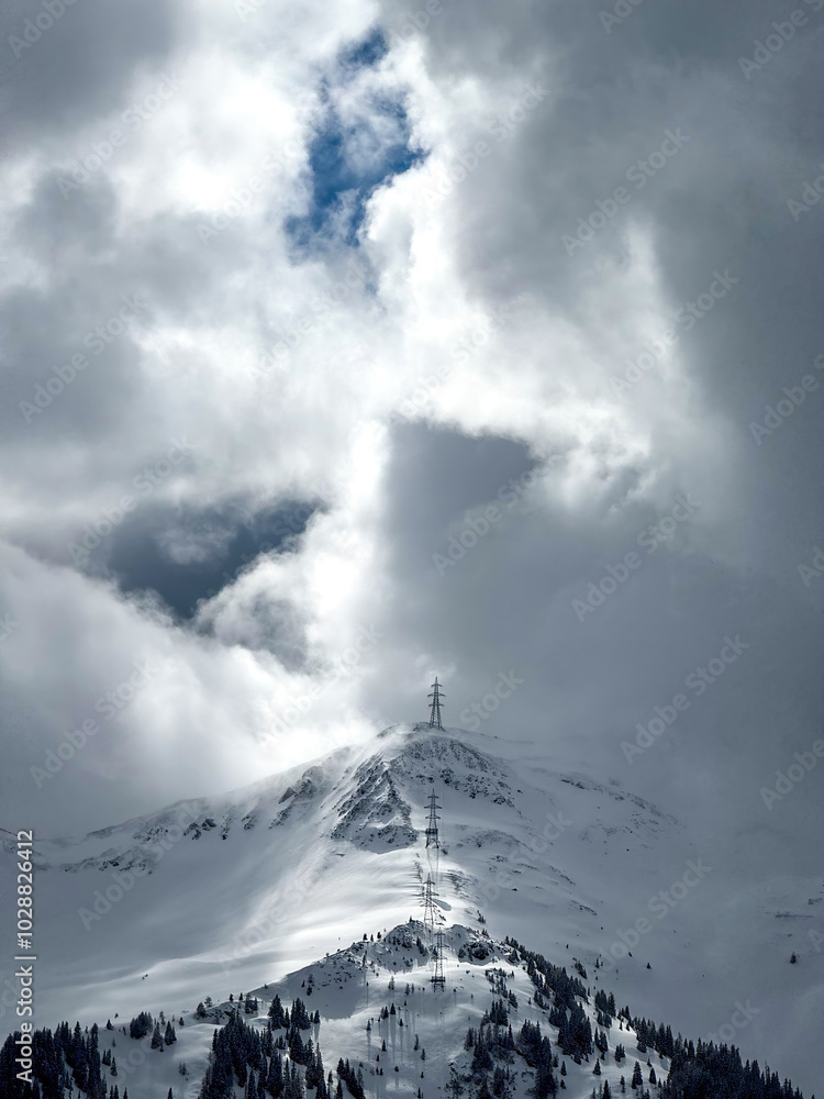 Electric power line runnnig up a snow covered mountain in the ski region of Saalbach-Hinterglemm, Austria against dramatic cloudy sky