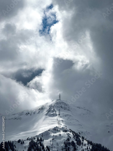 Electric power line runnnig up a snow covered mountain in the ski region of Saalbach-Hinterglemm, Austria against dramatic cloudy sky