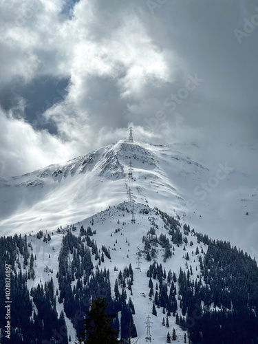 Obraz na płótnie Electric power line runnnig up a snow covered mountain with snow line at the bottom in the ski region of Saalbach-Hinterglemm, Austria against dramatic cloudy sky w salonie