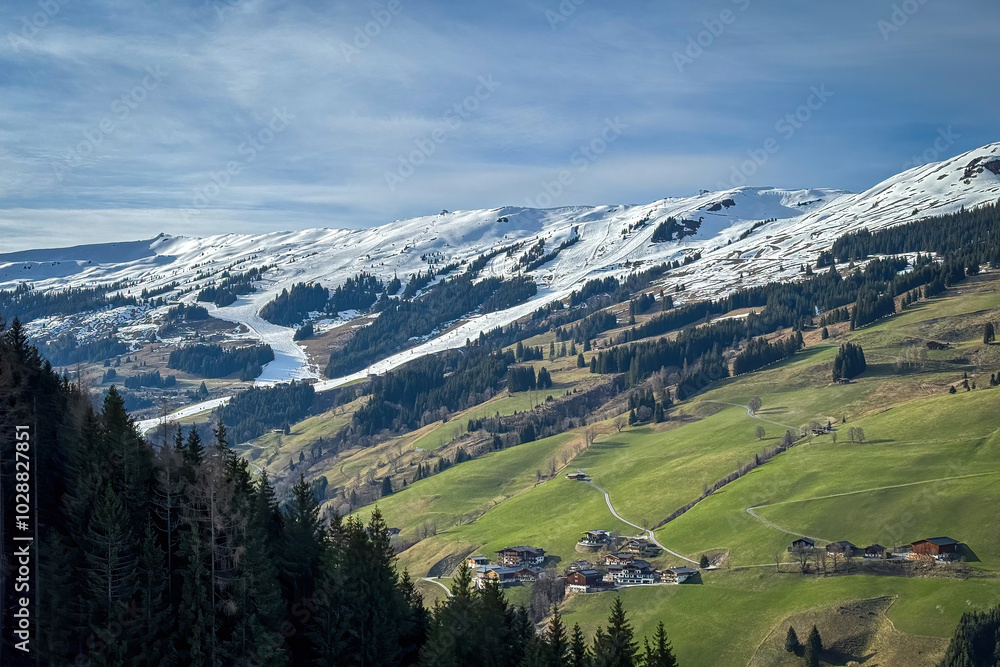 Scenic view of ski region of Saalbach-Hinterglemm with green meadows and slopes in bad conditions in the Austrian alps against blue sky with clouds in mid March 2024