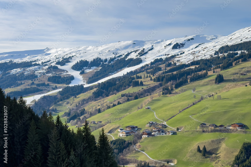 Scenic view of ski region of Saalbach-Hinterglemm with green meadows and slopes in bad conditions in the Austrian alps against blue sky with clouds in mid March 2024