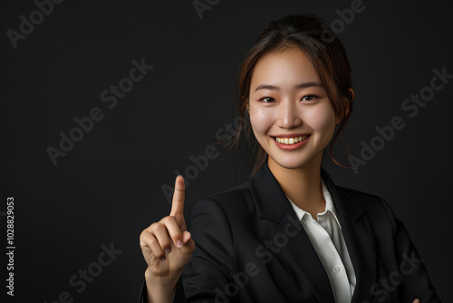 young Asian business woman smiling and pointing her finger to the side on a black background.