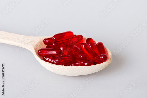 Vitamin capsules in a spoon on a colored background. Pills served as a healthy meal. Red soft gel vitamin supplement capsules on spoon photo