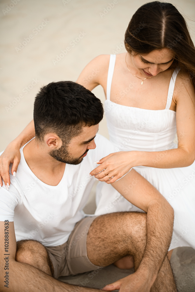 Close-up top view of young couple sitting on sand, girl putting her hands on guy's shoulders Close-up top view of young couple sitting on sand, girl putting her hands on guy's shoulders